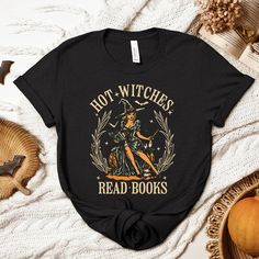 Thank you for visiting SuniDazeDesigns and supporting a small family owned business.  Embrace your inner bookworm with our retro Halloween shirt, featuring a vintage-inspired design of a witch engrossed in a spellbinding read. Perfect for those who know that intelligence is the ultimate enchantment, this 'Hot Witches Read Books' tee combines spooky style with a love for literature. Show off your bewitching charm and passion for reading this Halloween season. Please carefully read the following... HOW TO ORDER  Choose Your Size Choose Your Shirt Color Select the quantity Click Add To Cart For multiple items go back to the listing and repeat the steps. PLEASE MAKE SURE YOU HAVE READ AND UNDERSTAND THE DESCRIPTION FULLY BEFORE PLACING AN ORDER PRINTING The entire process is eco-friendly; inks Black Bookish Top With Letter Print, Black Letter Print Top For Bookish Style, Black Bookish Tops With Text Print, Fall Themed T-shirt With Letter Print, Black Bookish Top With Text Print, Bookish Halloween Graphic Print Top, Bookish Graphic Print Top For Halloween, Fall Bookish T-shirt With Letter Print, Bookish Fall T-shirt With Letter Print