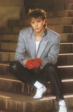 a young man sitting on steps with his hands in his pockets and wearing red gloves