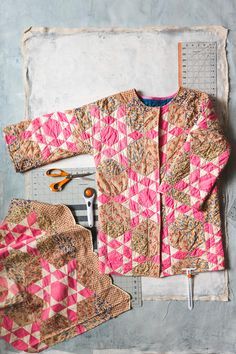 a pink and brown jacket sitting on top of a table next to other clothing items