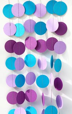 paper circles hanging from strings on a white wall with blue, purple and pink colors