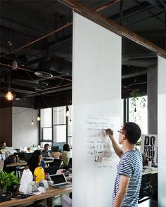 a man writing on a whiteboard in an office with people sitting at desks