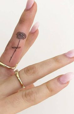 a woman's hand with a small flower tattoo on the middle finger and ring