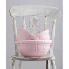 two pink bowls sitting on top of a white wooden chair next to a gray wall