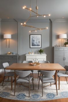 a dining room table and chairs with lights hanging from the ceiling above it in front of a dresser