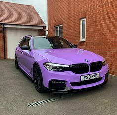 a purple bmw is parked in front of a brick building with two garage doors on the side