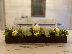 candles are lit in a wooden box with flowers and greenery on the table top