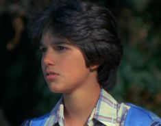 a young man with black hair wearing a blue shirt and bow tie looking off to the side