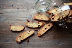 several pieces of bread and nuts on a wooden table next to a glass jar with almonds