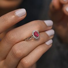 a woman's hand holding a ring with an oval shaped ruby stone surrounded by small white diamonds