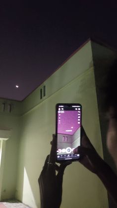 a person holding up a cell phone in front of a building with lights on it