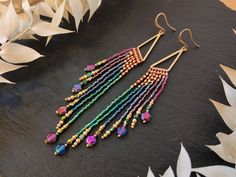 a pair of multicolored beaded earrings sitting on top of a black surface