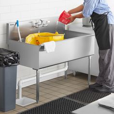 a man is washing his hands in the kitchen sink while holding a red and yellow container