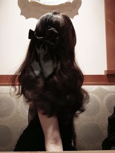 the back of a woman's head with a black bow in her hair sitting on a bench