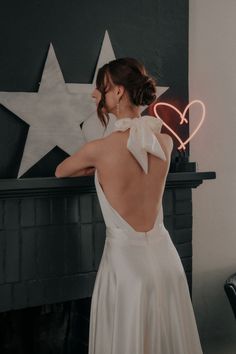 a woman standing in front of a fireplace with a heart shaped neon sign above her back