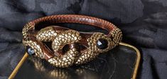 Absolutely stunning! Authentic Roberto Cavalli double headed snake bangle. This is a rare, collectible designer bracelet. In excellent condition with no visible flaws. Gold, brown with black stones. Gold metal, glass and enamel. Fits wrist up to 7 cm in diameter. Signed, made in Italy. Double Headed Snake, Snake Bangle, Designer Bracelet, Black Stones, Snake Bracelet, Black Stone, Roberto Cavalli, Bracelet Designs, Arm Band