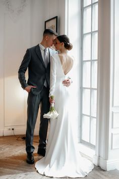 a bride and groom standing in front of a window