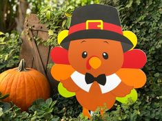 a turkey with a hat and bow tie standing in the bushes next to a pumpkin