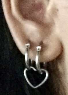 a pair of silver hoop earrings with a heart hanging from the middle of each ear