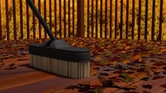 a broom sitting on top of a wooden floor covered in leaves next to a fence