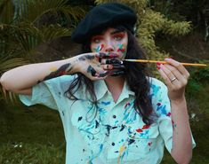 a woman with paint all over her face holding a brush and painting on her face