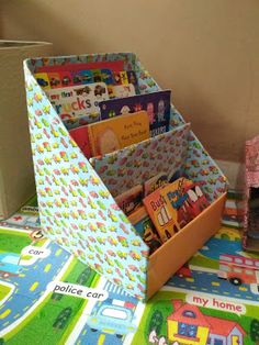 children's books and toys sit on the floor next to a cardboard box filled with them