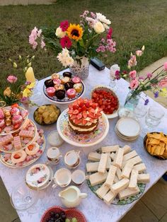 a table topped with lots of food on top of a grass covered field next to flowers