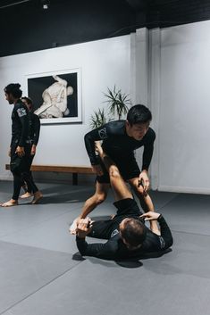 two men in black shirts and one is on the ground while another man holds his leg up