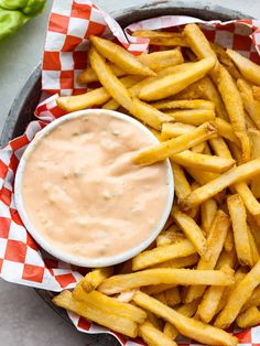 french fries with dipping sauce in a bowl on a checkered table cloth next to a green pepper