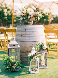 an outdoor ceremony setup with lanterns and flowers on the grass in front of a barrel