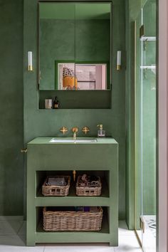 a green bathroom with two baskets under the sink and a large mirror above it on the wall