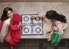 two women playing a board game on the sidewalk outside their home in india, top view from above