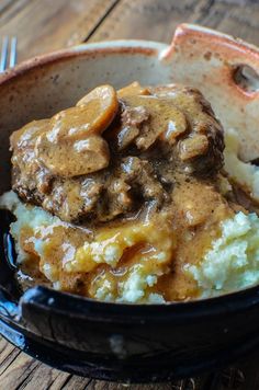 a bowl filled with mashed potatoes covered in meat and gravy on top of a wooden table