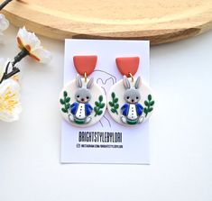 the earrings are decorated with rabbits and plants on them, sitting next to a card