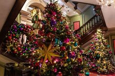 a christmas tree in the middle of a room with many ornaments on it and stairs