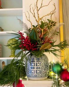 a blue and white vase filled with greenery on top of a mantle next to christmas decorations