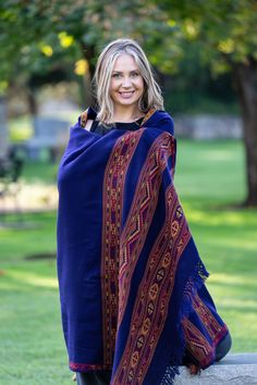 a woman wearing a blue shawl and black boots posing for a photo in the park