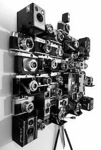 a bunch of old cameras are hanging on the wall next to a camera tripod