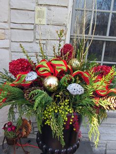 a vase filled with red flowers and greenery on top of a table next to a window