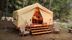 a tent set up in the woods with two chairs and steps leading to it, next to a river