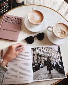 a person reading a book next to two cups of coffee