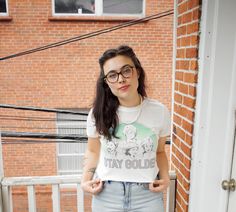 a young woman wearing glasses standing in front of a brick wall with her hands on her hips