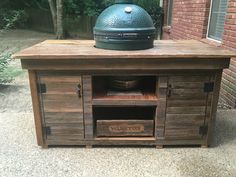 a big green egg sitting on top of a wooden table next to a brick building