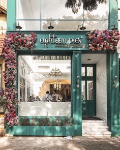 the front entrance to eighteen pies with flowers on it's display window and people sitting at tables outside