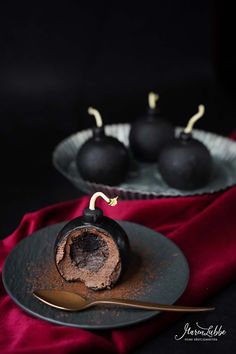 some chocolate desserts are on a black plate with a gold spoon and red cloth