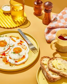 two eggs and toast sit on a yellow plate next to a cup of tea, butter and honey