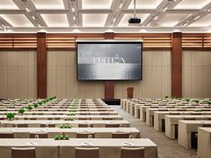 an empty conference room with tables and chairs in front of a large screen on the wall