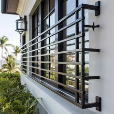 a window on the side of a white building with black metal bars hanging from it's sides