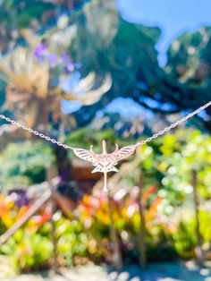 a small white bird is hanging from a string in the air with trees and bushes behind it