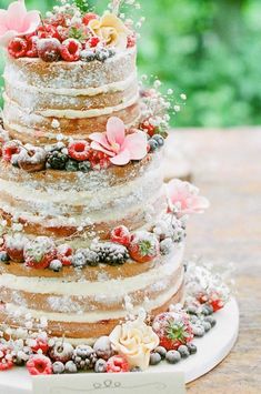 a multi layer cake with flowers and berries on the top is sitting on a plate