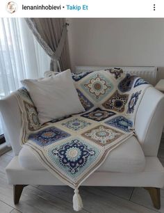 a white couch with a blue and brown blanket on it's back in front of a window